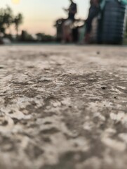 Low angle view of textured ground with blurred figures in the background at sunset
