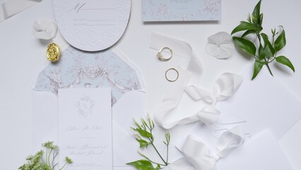 Wedding invitation suite with rings, ribbon, and greenery on a white background. Action