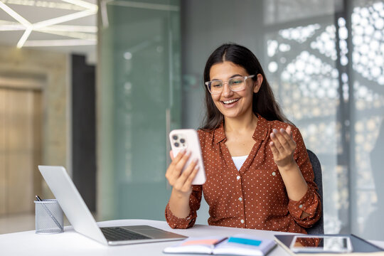 Young professional woman smiling and gesturing while communicating on a video call using her smartphone, working remotely or connecting online from a contemporary office environment