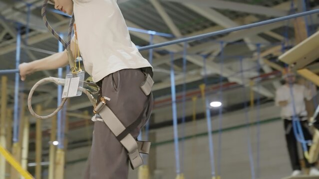 Young boy wearing safety equipment navigating rope bridge in indoor adventure park. Creative