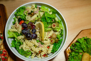 Cold pasta salad with pasta, lettuce, olives, tuna, grapes and finely chopped vegetables