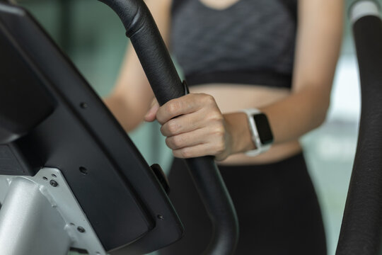 Close up of woman hand gripping elliptical machine handle while wearing smart fitness watch. Concept of workout tracking, cardio exercise, fitness technology and health monitoring in gym.