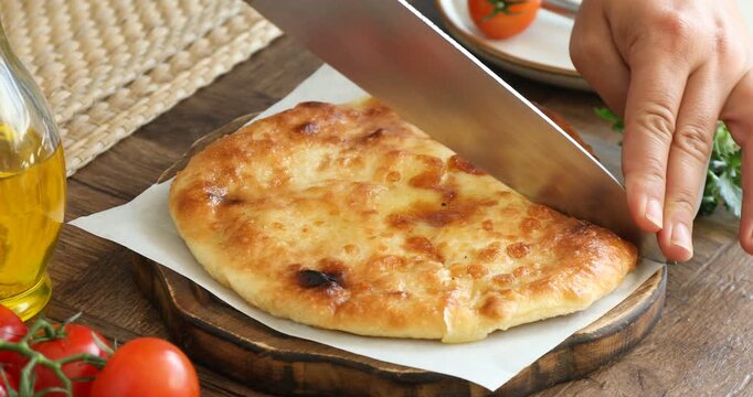 Woman cutting delicious Megrelian khachapuri at wooden table, closeup