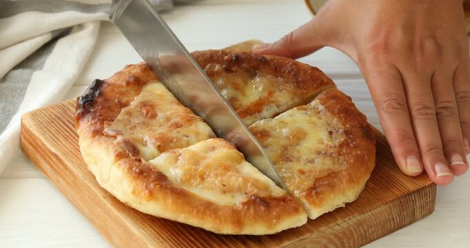 Woman cutting delicious Megrelian khachapuri at white wooden table, closeup