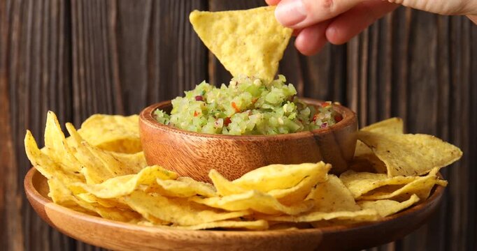 Woman dipping nacho into tasty salsa at spinning table, closeup