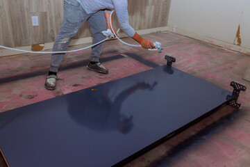 Painter applies smooth coat of navy paint to large tabletop, revealing fresh look in renovated room.