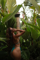 Woman in turquoise bikini standing among tropical plants, natural light and lush greenery