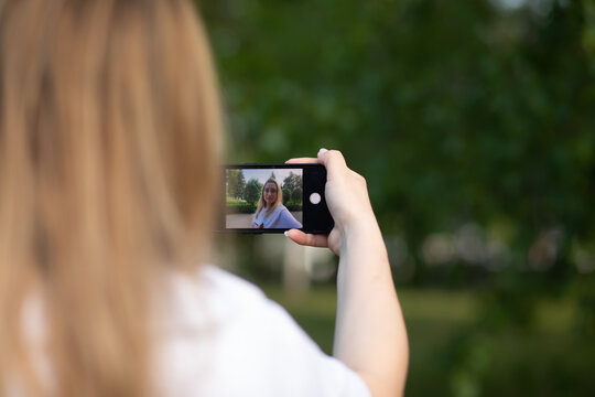 Pretty woman taking selfie with mobile phone looking at camera in a park. Blogger recording video vlog.