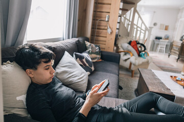 Teenager girl lying on a sofa and using a smartphone in a bright and cozy living room