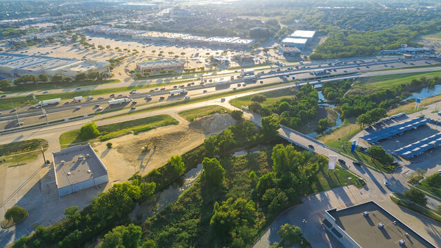 Car dealership with covered outdoor parking in Lewisville, Texas, flat-roof commercial buildings with rooftop HVAC units, and busy highway interchange surrounded by industrial and service zones