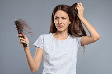Woman with brush and lost hair on grey background. Alopecia problem