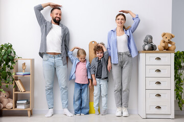 Parents and children measuring their heights near white wall at home