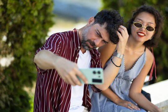 Couple taking a selfie outdoors, enjoying a sunny day together and capturing memories with a smartphone - Powered by Adobe