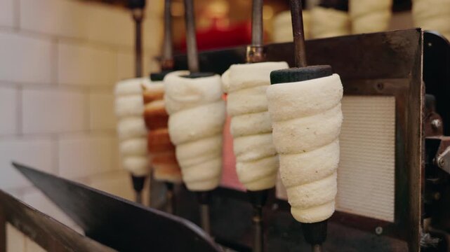 Traditional Czech Trdelnik pastry baking on rotating spits over an open heat source at a street market in Prague.