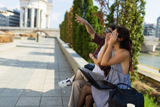 Young couple exploring city sights on a sunny day, pointing at landmarks, enjoying outdoor adventure and urban exploration