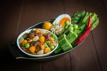 Top-view still life of authentic Nam Prik Long Ruea, a traditional Thai chili paste dip, presented in ceramic bowls on a wooden board and banana leaf. The composition includes fresh seasonal vegetable