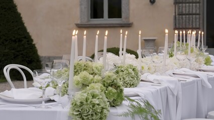 Elegant white table setting with lighted candles and green hydrangeas centerpieces. Action