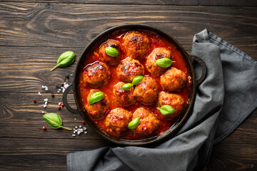 Meatballs in tomato sauce with basil leaves on wooden table.