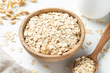 Rolled oats in wooden bowl with golden ears on white background.