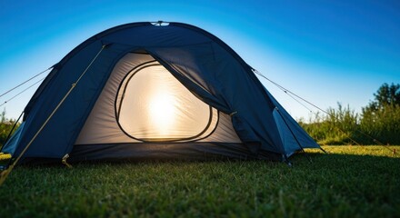 Dark blue tent on grassy field, sunrise shining through open doorway