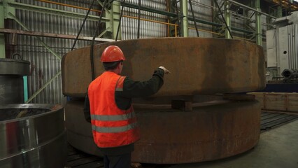 Industrial worker supervising heavy metal component lifting in factory. Stock clip