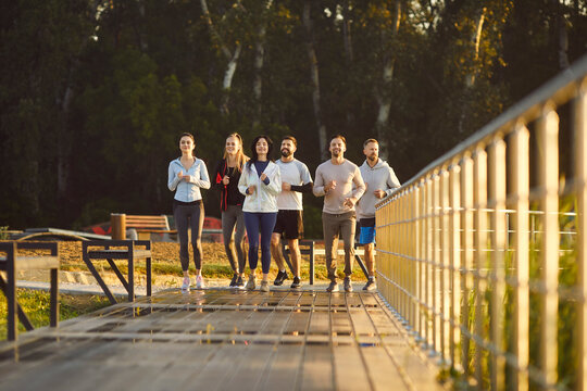 Group of people runs together outdoors during team workout, boosting running effort, uniting in jogging sport, enhancing fitness jog training, engaging in a lively open-air exercise session.