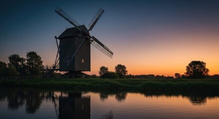 Old wooden windmill at sunset, reflected in calm river