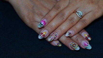 A close-up of a woman's hand featuring festive Diwali-themed nail art. The design includes traditional Indian elements such as diyas, rangoli patterns, glitter, and vibrant colors like gold, red, and 