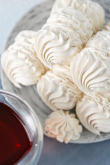 Delicate meringue cookies arranged on a plate, accompanied by a glass of tea, with decorative spices and tea tins in the background, creating a cozy dessert scene