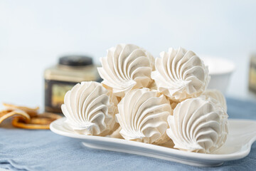 Delicate meringue cookies arranged on a plate, accompanied by a glass of tea, with decorative...