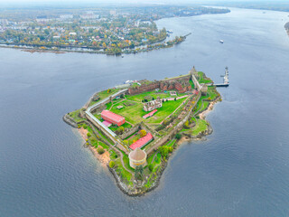 Wide aerial panoramic view of the Oreshek Fortress island in the center, with the water and the distant town in the background