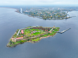 Wide aerial panoramic view of the Oreshek Fortress island in the center, with the water and the distant town in the background