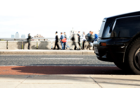 London Rush Hour: A black London taxi waiting for a fare during rush hour while commuters and pedestrians pass by on a London Bridge pavement. 