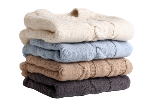 Stack of four folded cable knit sweaters in cream blue tan and grey isolated on a transparent background