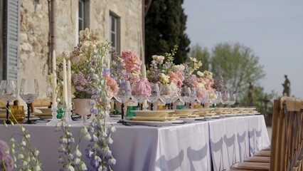 Elegant wedding table setting with floral centerpieces in front of a stone house. Action