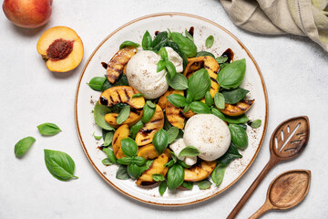 Mediterranean salad with burrata cheese, grilled peaches, fresh basil leaves, olive oil and balsamic glaze, gourmet summer dish on light background