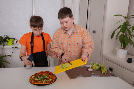 Kids cooking together in a kitchen while preparing a pizza topped with fresh vegetables - Powered by Adobe