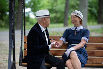 Elderly couple sitting on a bench in a park, enjoying a conversation and holding hands in the afternoon sun