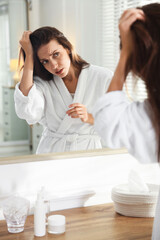 Woman with hair loss problem looking i mirror at home