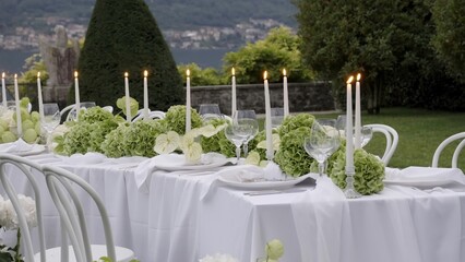 Elegant white table setting with candles and flowers in garden. Action