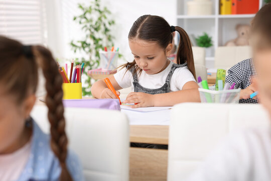 Cute little girl drawing at wooden desk during art lesson in elementary school