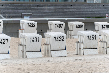 Numbered white beach chairs stand in rows on the sandy shore, waiting for visitors. The scene feels quiet and off-season.