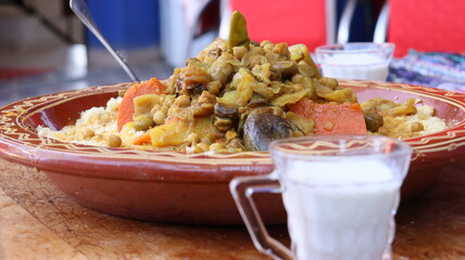 Traditional Moroccan couscous with vegetables and fermented milk (lben) — rustic tagine plate on wooden table, close-up with blue background