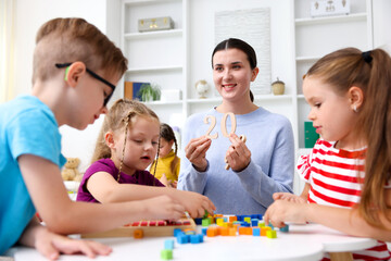 Fototapeta premium Cute children and smiling teacher at white table during lesson in elementary school