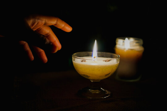 Woman's hand reaching toward a glowing candle in the dark, symbolizing hope, mindfulness, inner peace, and compassion