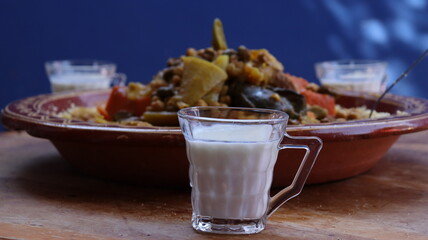 Traditional Moroccan couscous with vegetables and fermented milk (lben) — rustic tagine plate on wooden table, close-up with blue background