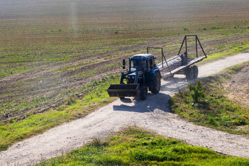 Blue Tractor Driving on Farm Track with Implement Near Plowed Field