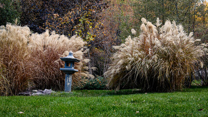Decorative stone lantern surrounded by golden ornamental grasses in autumn zen garden, natural landscape design