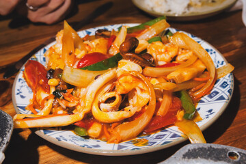 Stir frying fresh squid, shrimp, and colorful vegetables, including peppers, onions, and mushrooms, served in a traditional patterned plate for a delicious asian dining experience in hanoi
