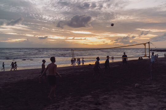 Men playing volleyball on the beach at sunset, silhouettes outlined by golden sky, representing teamwork, vitality, and joy in movement under warm evening light - Powered by Adobe